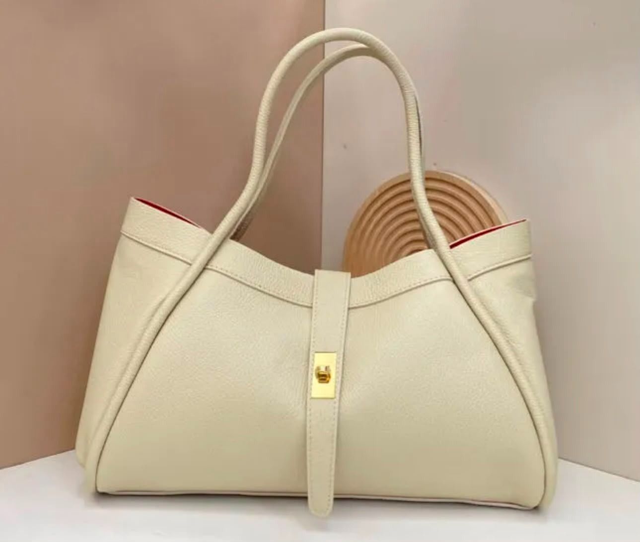 Bolso tote color crema con asas color camel y cierre dorado, mostrado sobre un fondo beige.