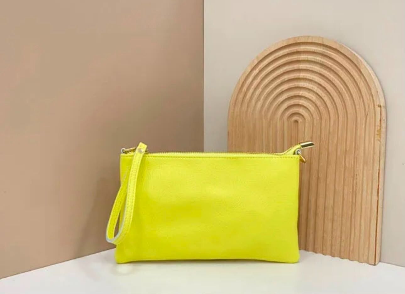 Un bolso de mano amarillo neón sobre una superficie blanca junto a una pieza decorativa de madera en forma de arco.