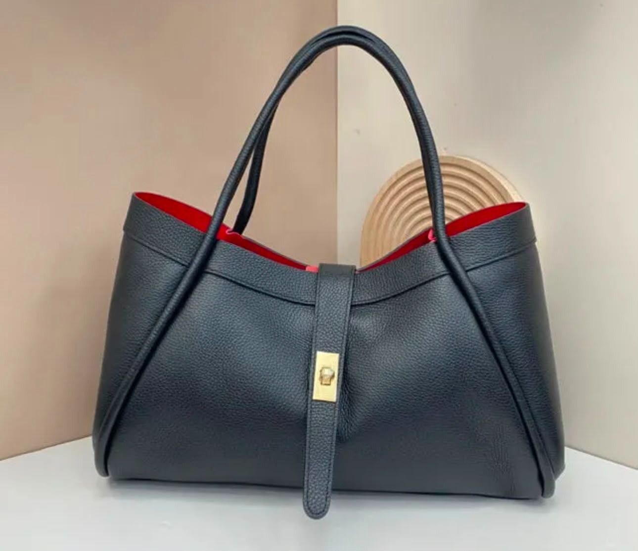 Bolso azul marino texturizado con asas superiores, forro rojo y cierre dorado sobre fondo claro.