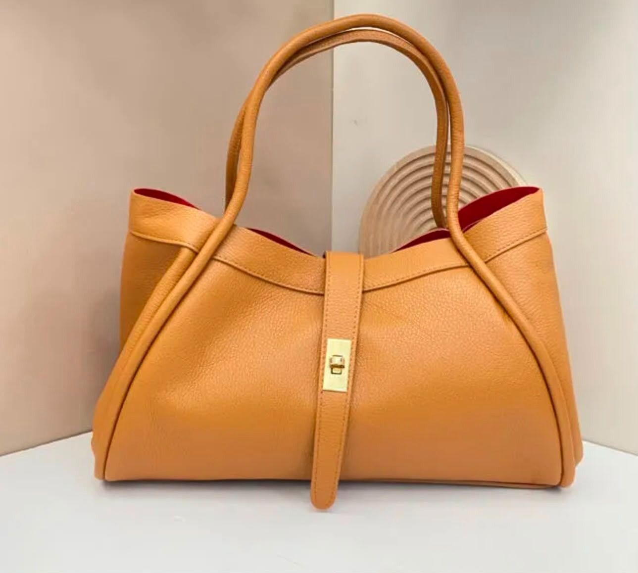 Bolso de mano de piel color camel con doble asa y cierre dorado, mostrado sobre un fondo claro.