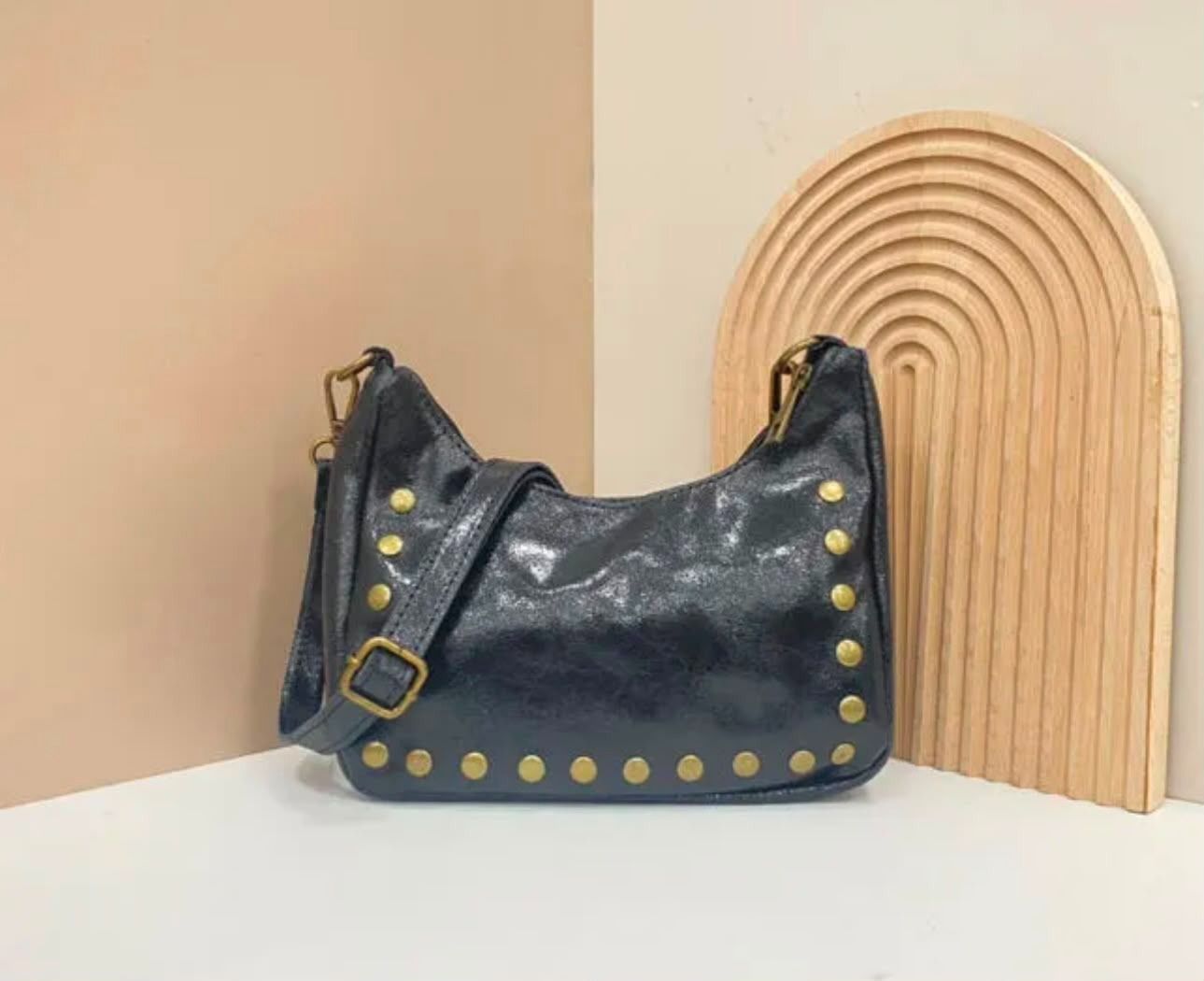 Un bolso negro con tachuelas sobre una superficie blanca junto a un arco decorativo de madera.