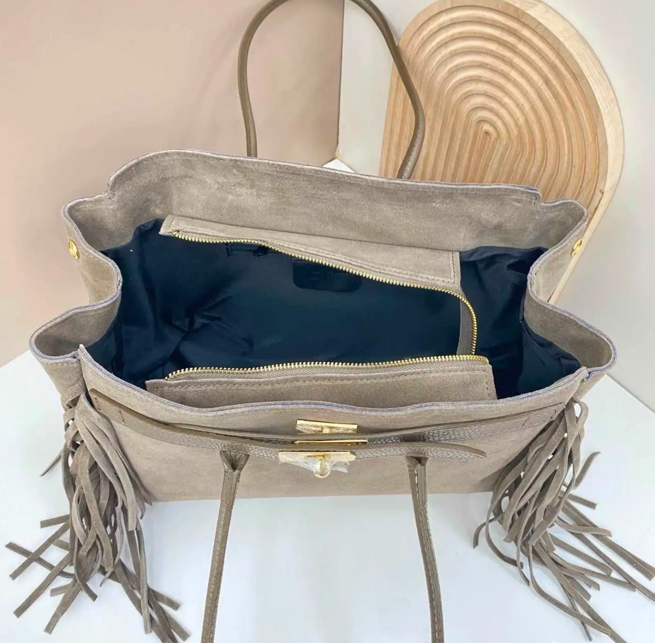 Bolso abierto gris con flecos, forro azul y sombrero de paja tejido detrás.