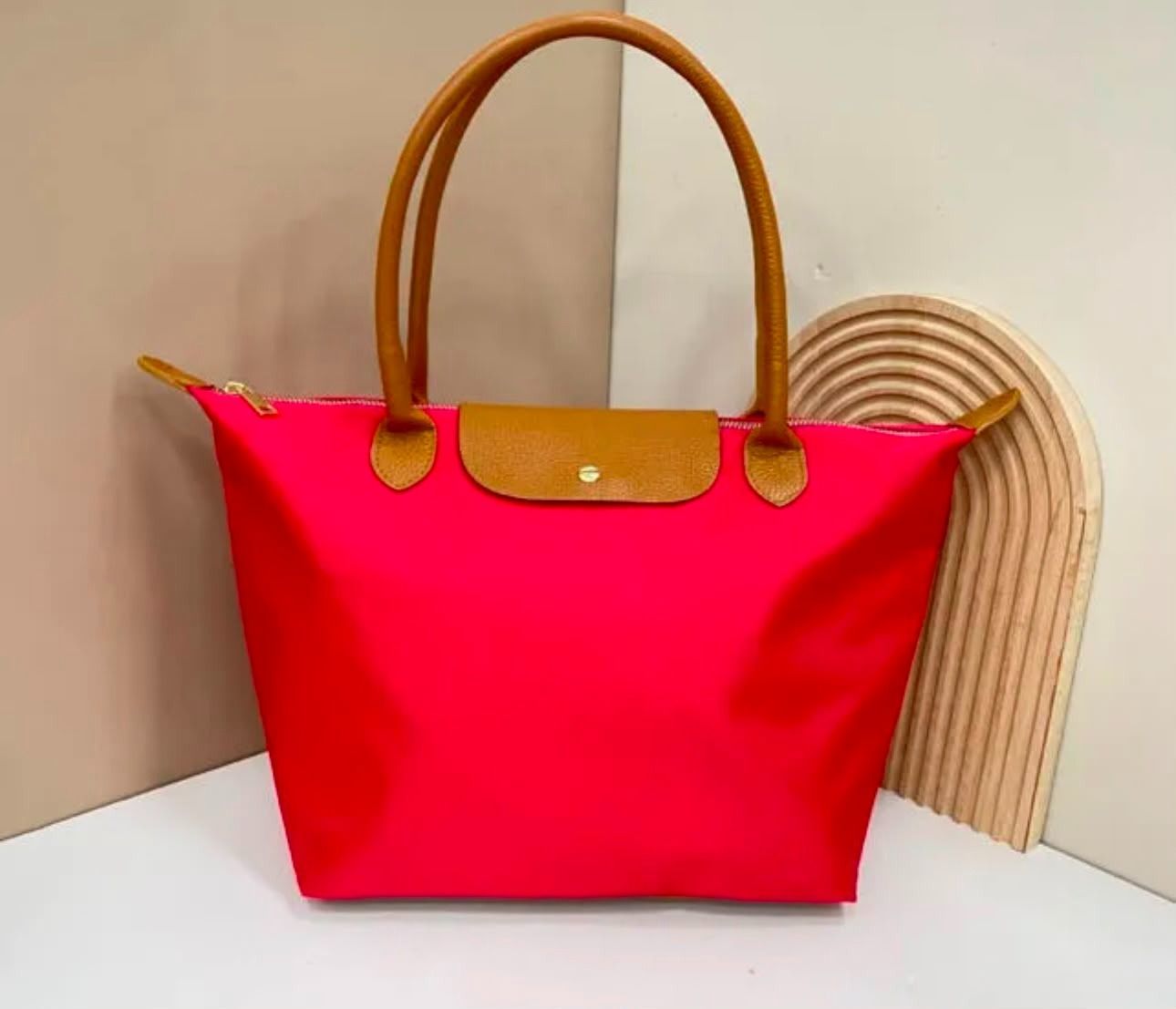 Bolso tote rosa brillante con asas color canela sobre una superficie blanca contra un fondo de esquina beige.