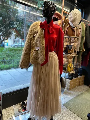 Maniquí en el escaparate de una tienda con blusa roja, falda de tul color crema y chaqueta de piel sintética color canela.