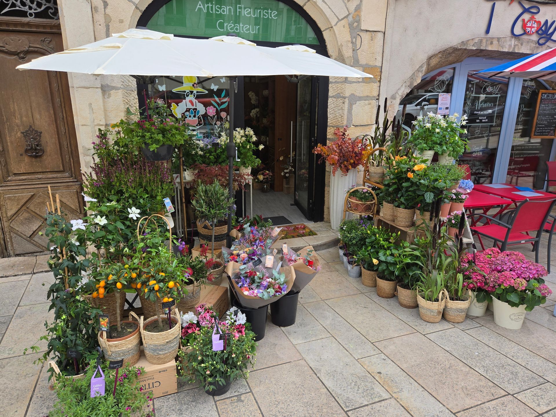 Présentoir extérieur de fleuriste avec plantes en pot et fleurs colorées sous un parasol blanc