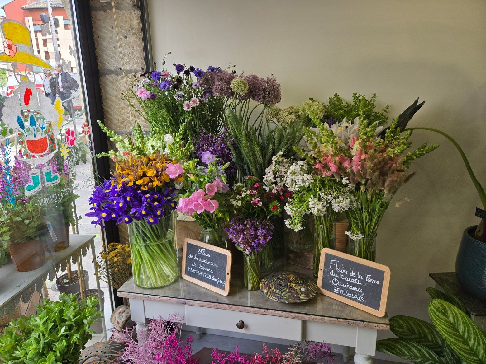 Vitrine de fleuriste avec des bouquets colorés dans des vases en verre et de petites ardoises