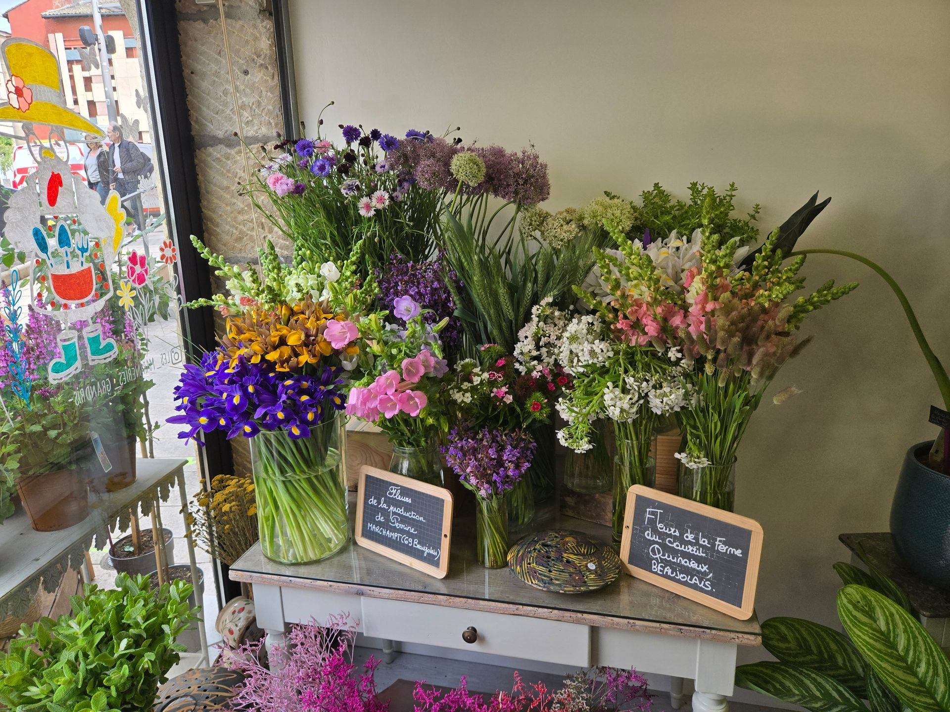 Vitrine de fleuriste avec des bouquets colorés dans des vases en verre et de petites ardoises
