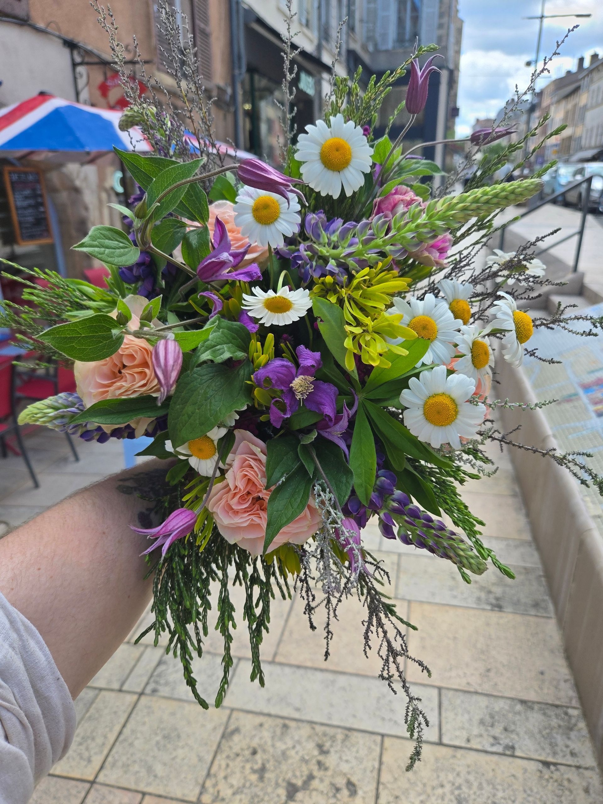 Bouquet de fleurs sauvages à la main, composé de marguerites, de fleurs violettes et de verdure, sur un trottoir de la ville