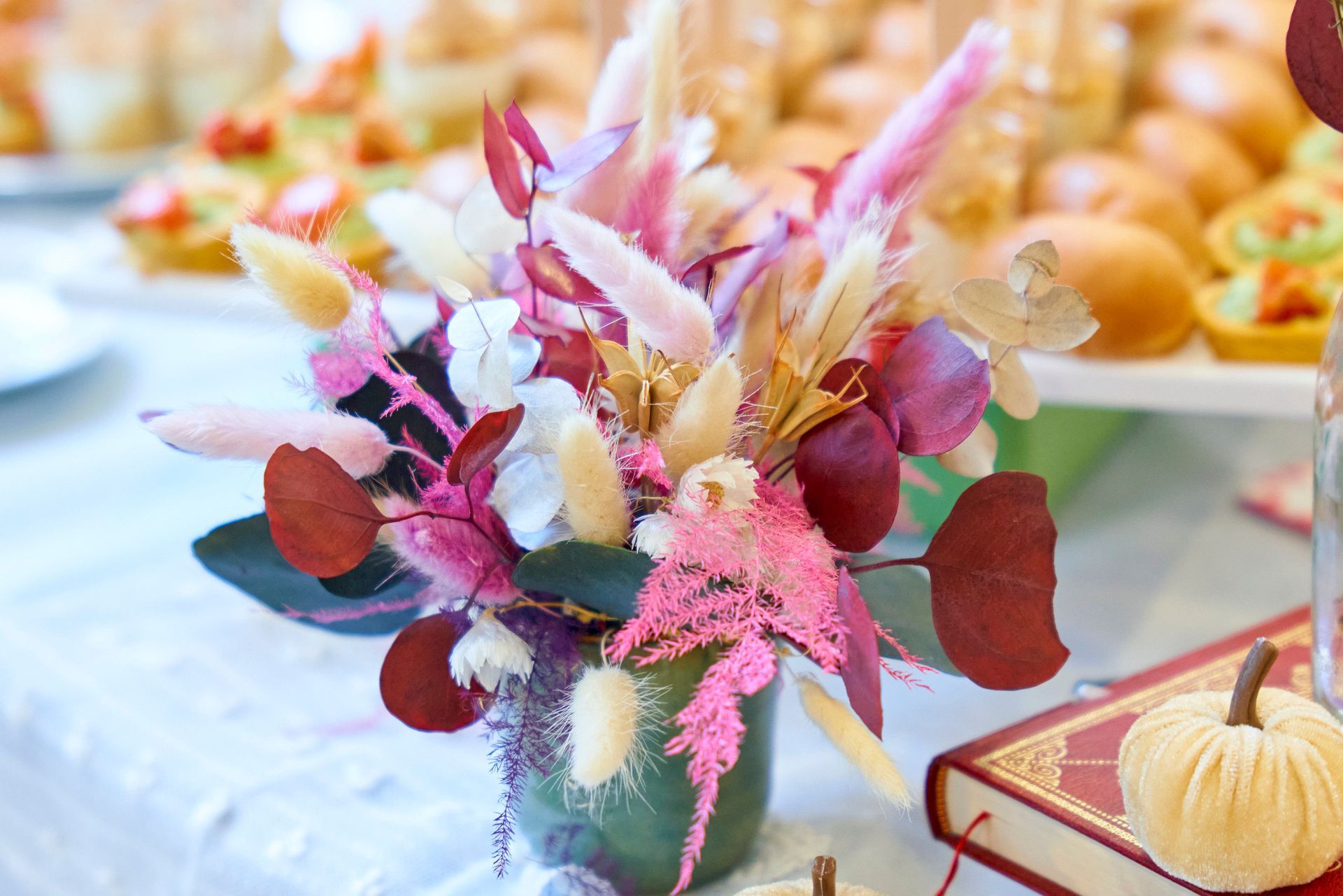 Composition florale rose et rouge dans un vase sur une table, avec des pâtisseries floues en arrière-plan.
