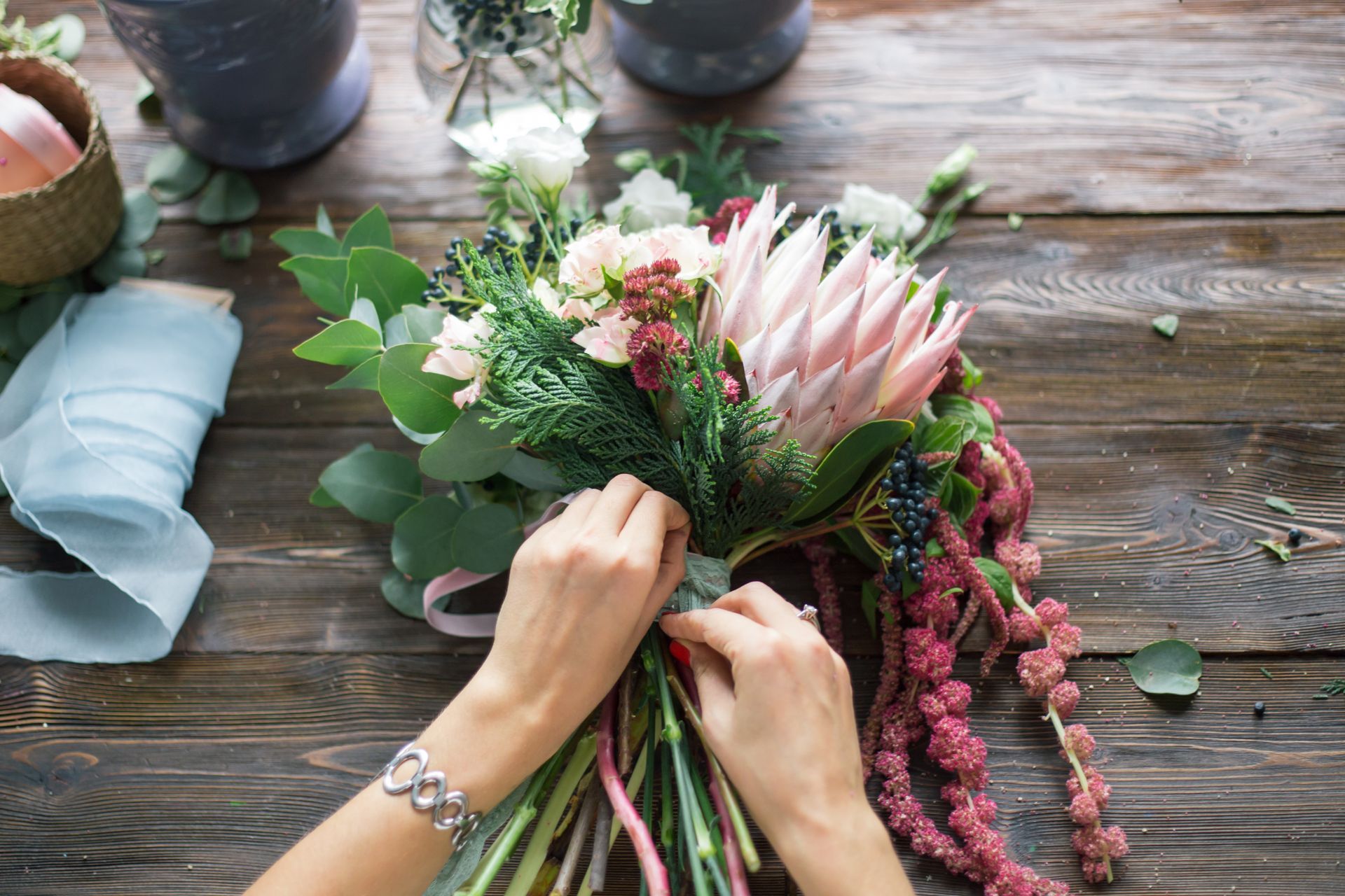 Des mains arrangent un bouquet de fleurs roses et vertes sur une table en bois rustique