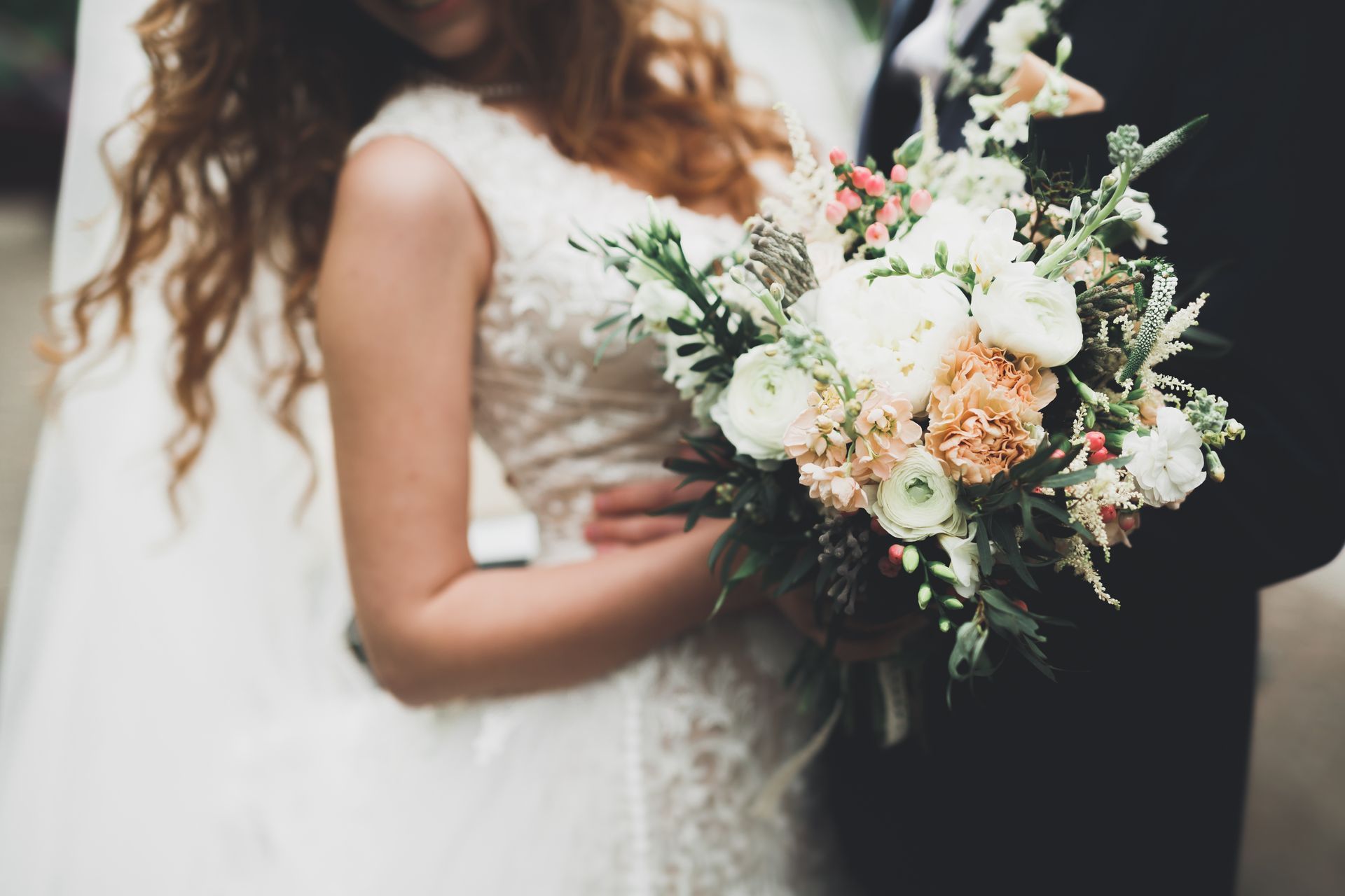 Une mariée tenant un bouquet de fleurs blanches et pêche à côté d'une personne en costume sombre