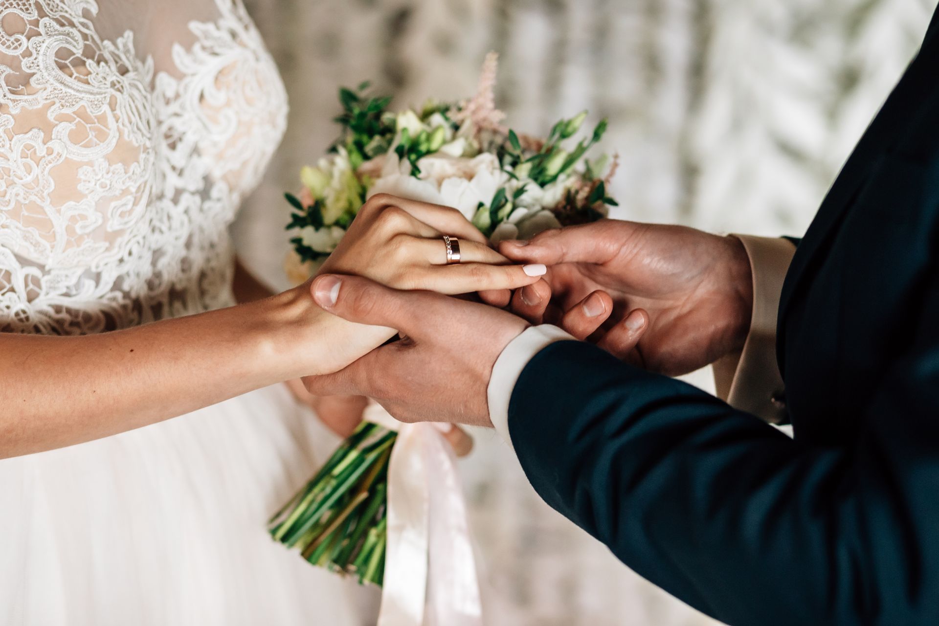 Des mains qui échangent des alliances près d'un bouquet de mariée et d'une robe de dentelle blanche
