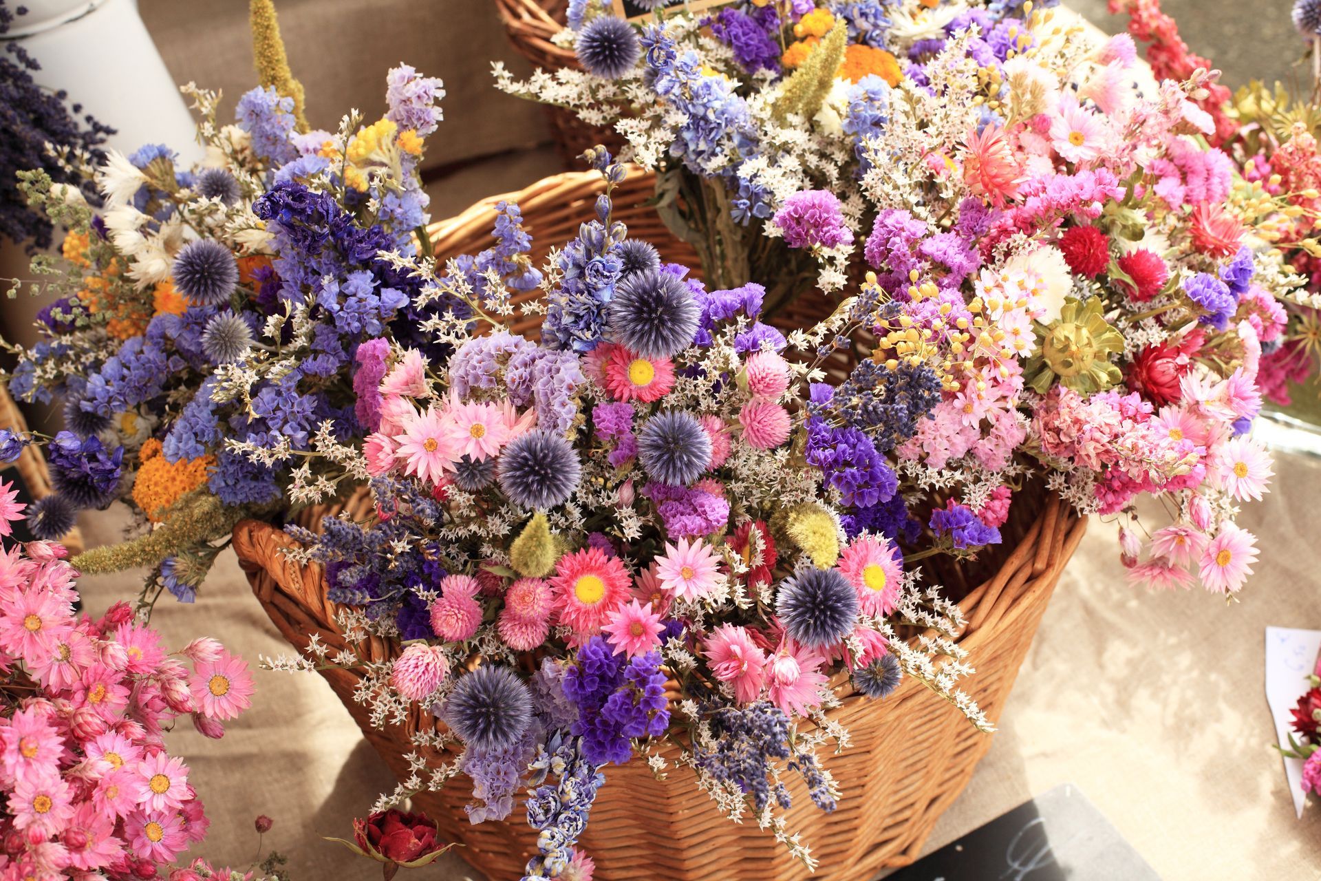 Paniers de fleurs séchées colorées, aux teintes violettes, roses, jaunes et blanches, présentés sur un étalage de marché lumineux.