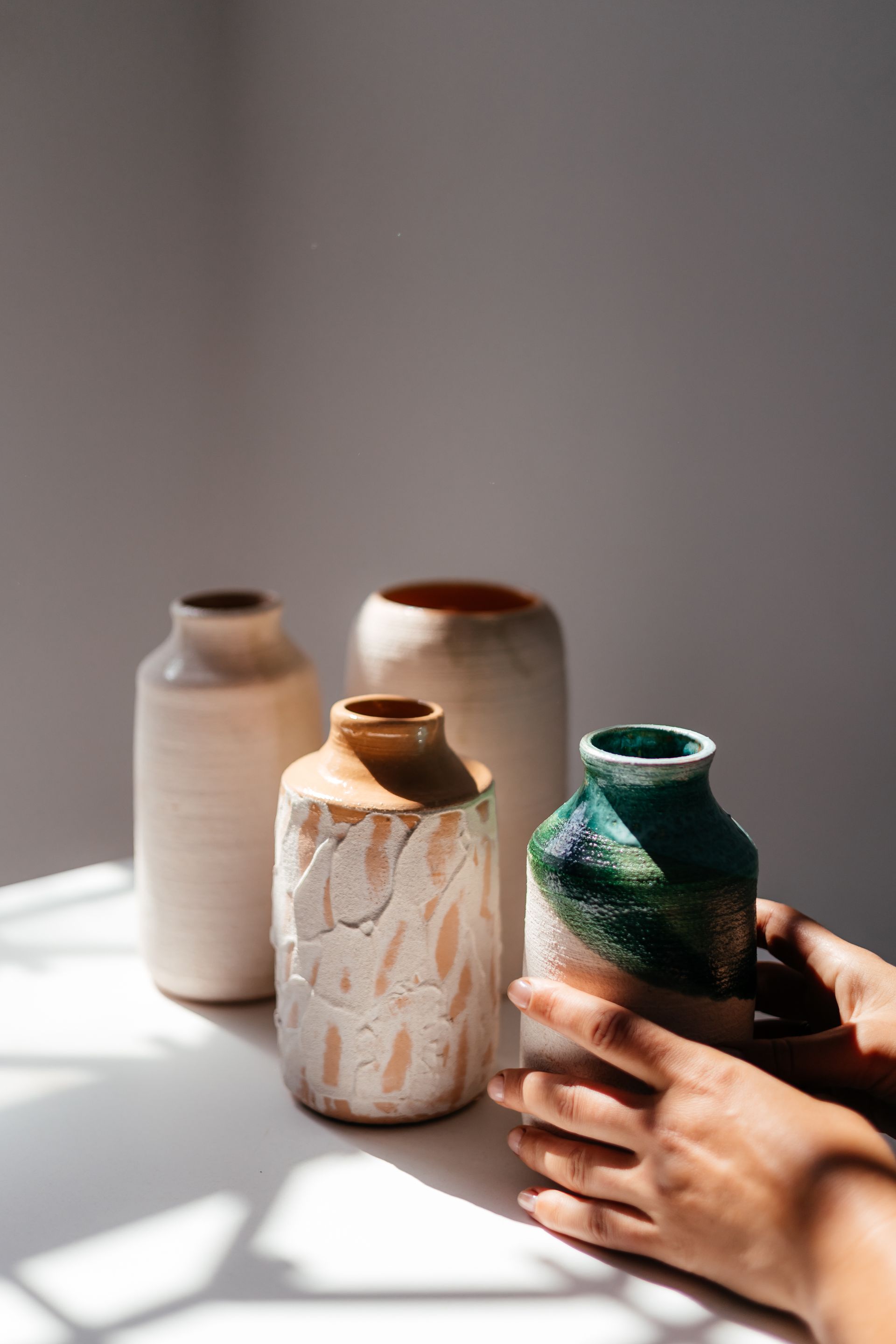 Des mains disposent trois petits vases en céramique sur une table ensoleillée
