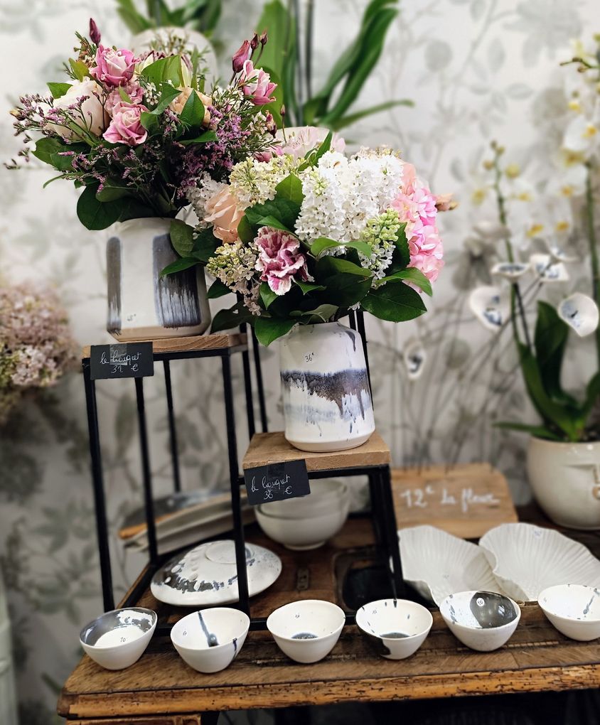 Des compositions florales roses et blanches dans des vases sur des présentoirs à étages, avec de petits bols blancs disposés en dessous.