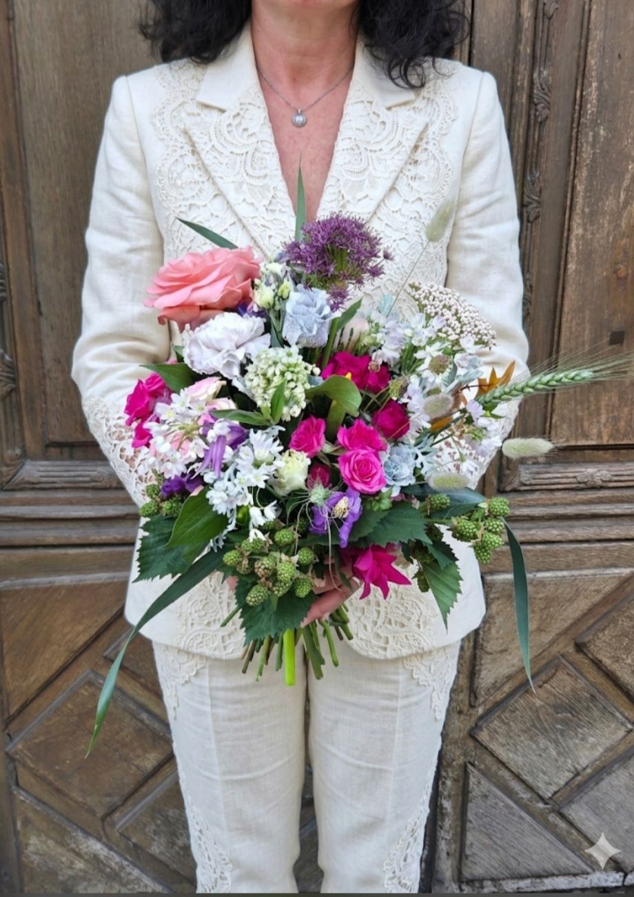 Une personne en tailleur crème tenant un bouquet coloré de fleurs roses, blanches et violettes