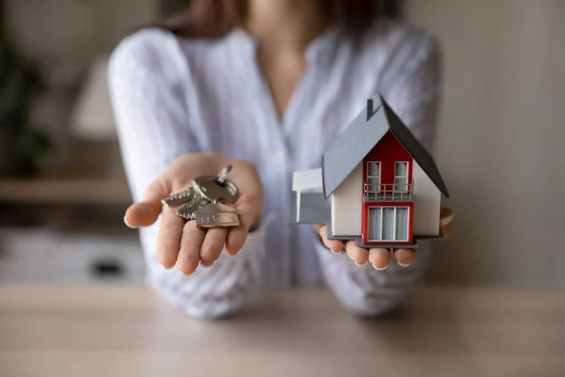 Persona sosteniendo maqueta de casa y llaves, en interior.