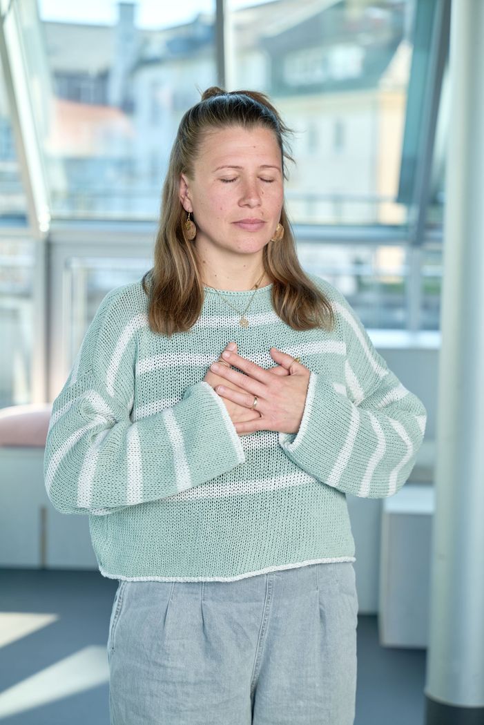 Eine Frau in einem Pullover hält ihre Brust mit den Händen.