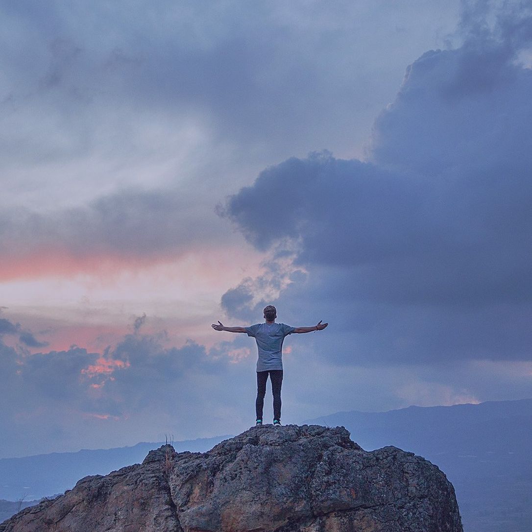 Ein Mann steht mit ausgestreckten Armen auf einem Berggipfel.