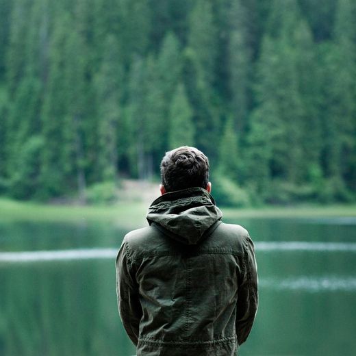 Ein Mann in einer grünen Jacke steht vor einem See.