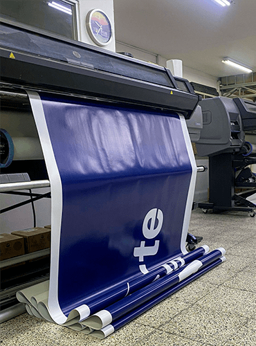 Impresora de gran formato imprimiendo una pancarta azul y blanca en interiores.