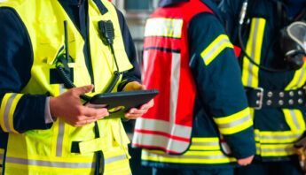 Personal de emergencia con chalecos reflectantes, uno usando una tableta y otros con equipo de extinción de incendios.