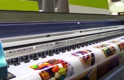 Impresora de gran formato que imprime imágenes coloridas en un rollo de material brillante.