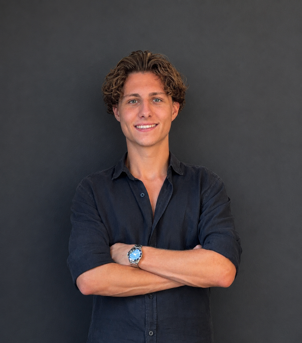 Smiling person in a dark shirt with arms crossed against a dark gray background