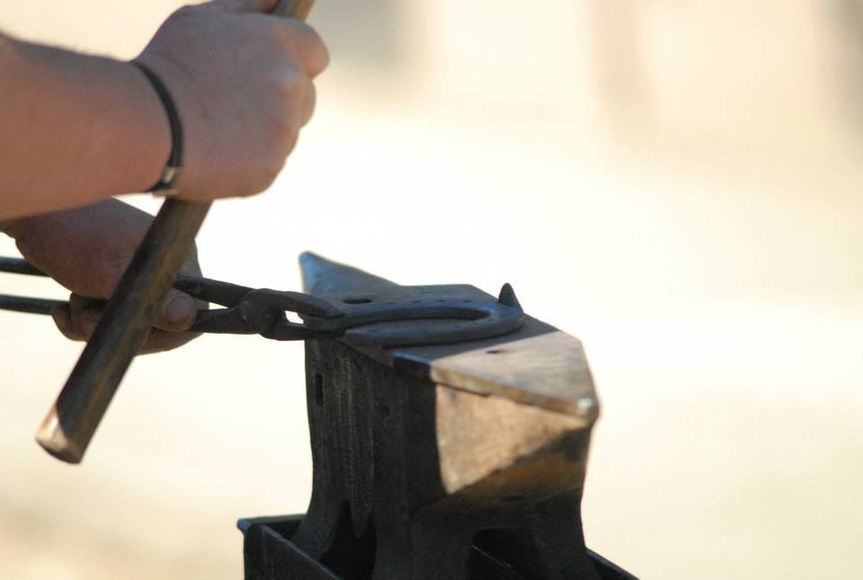 Maréchal-ferrant clouant un fer à cheval sur le sabot du cheval, détail de l'outil et de la main.