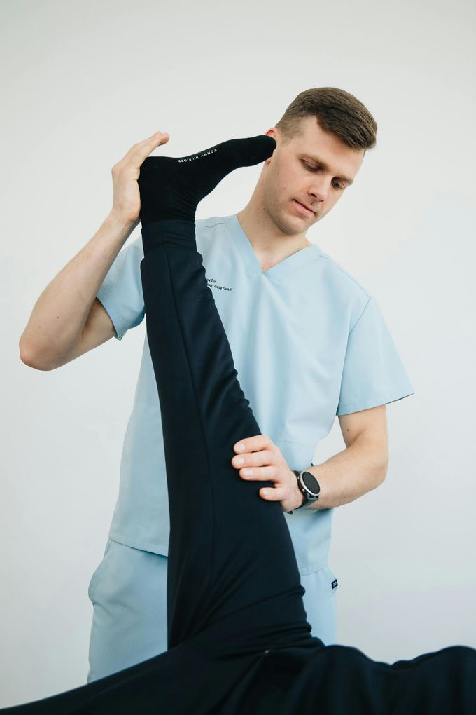 Fisioterapeuta estirando la pierna elevada de un paciente en un entorno clínico.