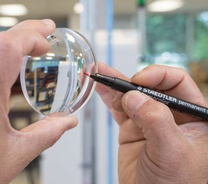 Une personne marque une lentille de verre transparente avec un feutre rouge.