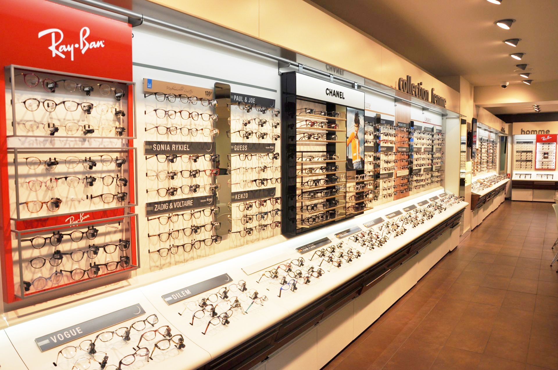 Intérieur du magasin d'Optique Pellé Krys : mur d'exposition présentant diverses montures, enseigne Ray-Ban et comptoir avec d'autres lunettes.