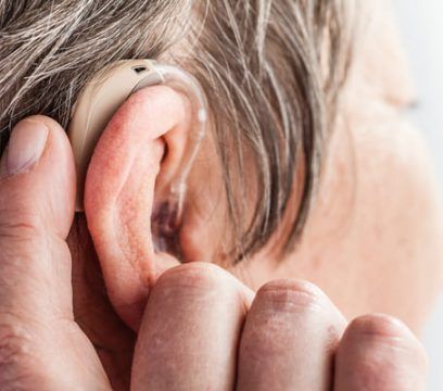 Personne ajustant un appareil auditif beige derrière son oreille.