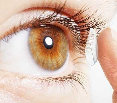 Œil à iris brun ; doigt tenant la lentille de contact, prête à être insérée.