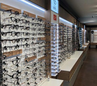 Des lunettes exposées sur des étagères dans un magasin d'optique lumineux. Éléments en bois et surfaces blanches.