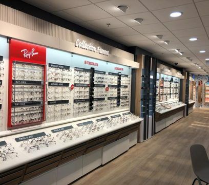 Intérieur d'un magasin d'optique présentant divers modèles de lunettes de vue et de soleil sur des étagères et dans des vitrines.