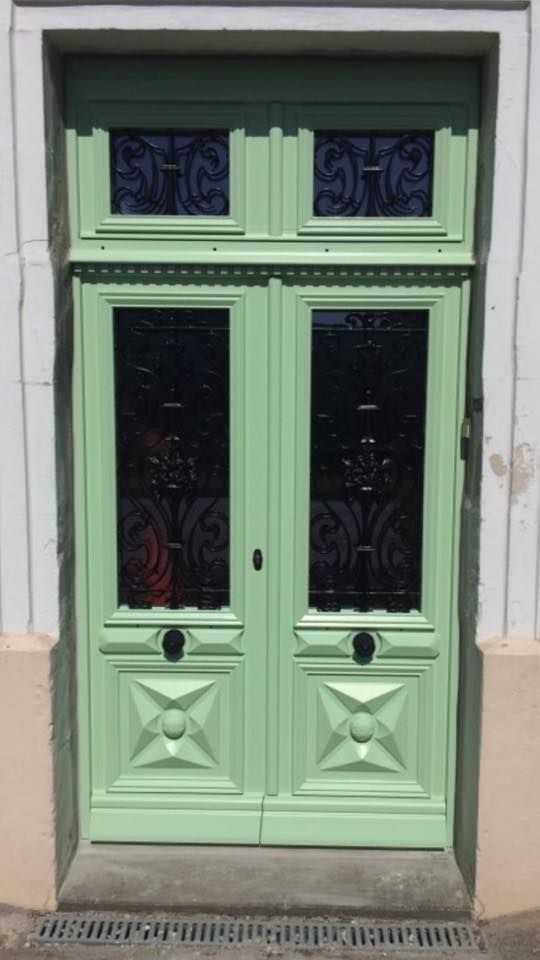 Porte double verte avec panneaux de verre décoratifs et une garniture ornée.