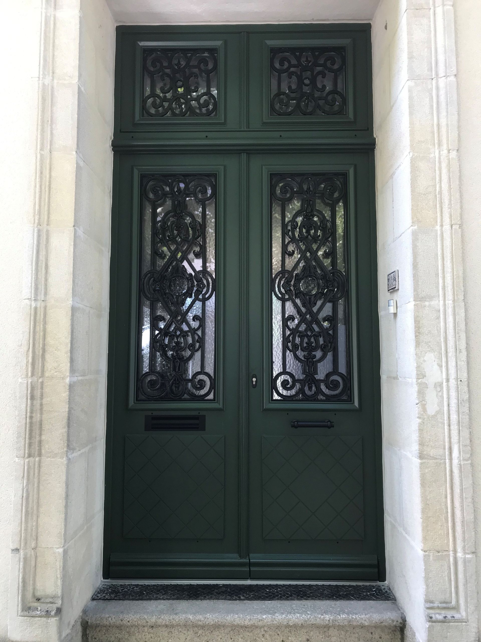 Portes doubles vertes avec détails en fer forgé noir.