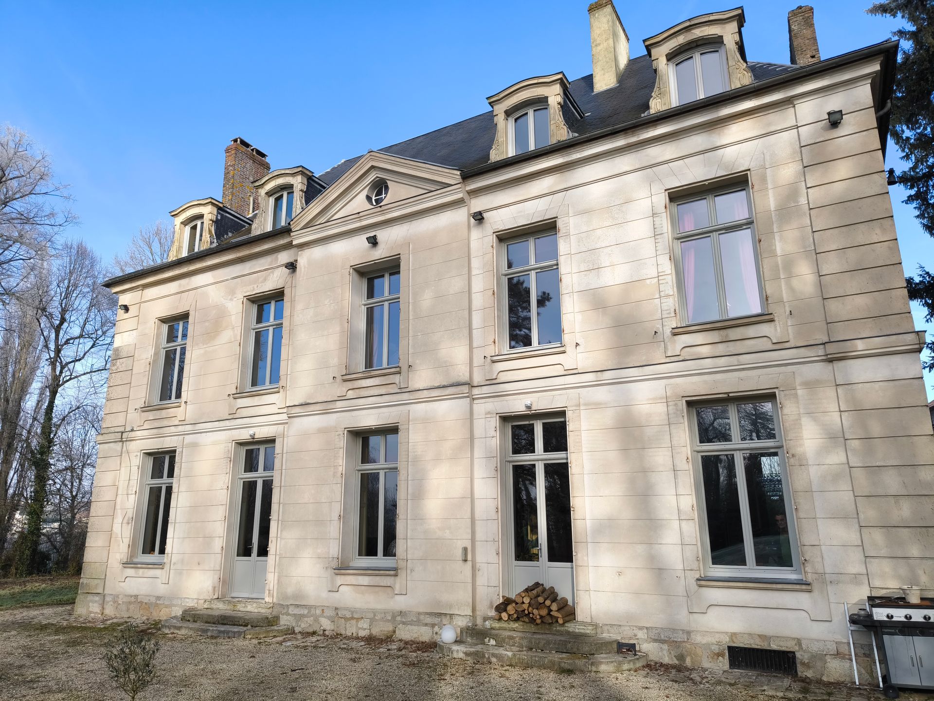 Bâtiment en pierre de deux étages avec de nombreuses fenêtres, un toit sombre et un ciel ensoleillé.