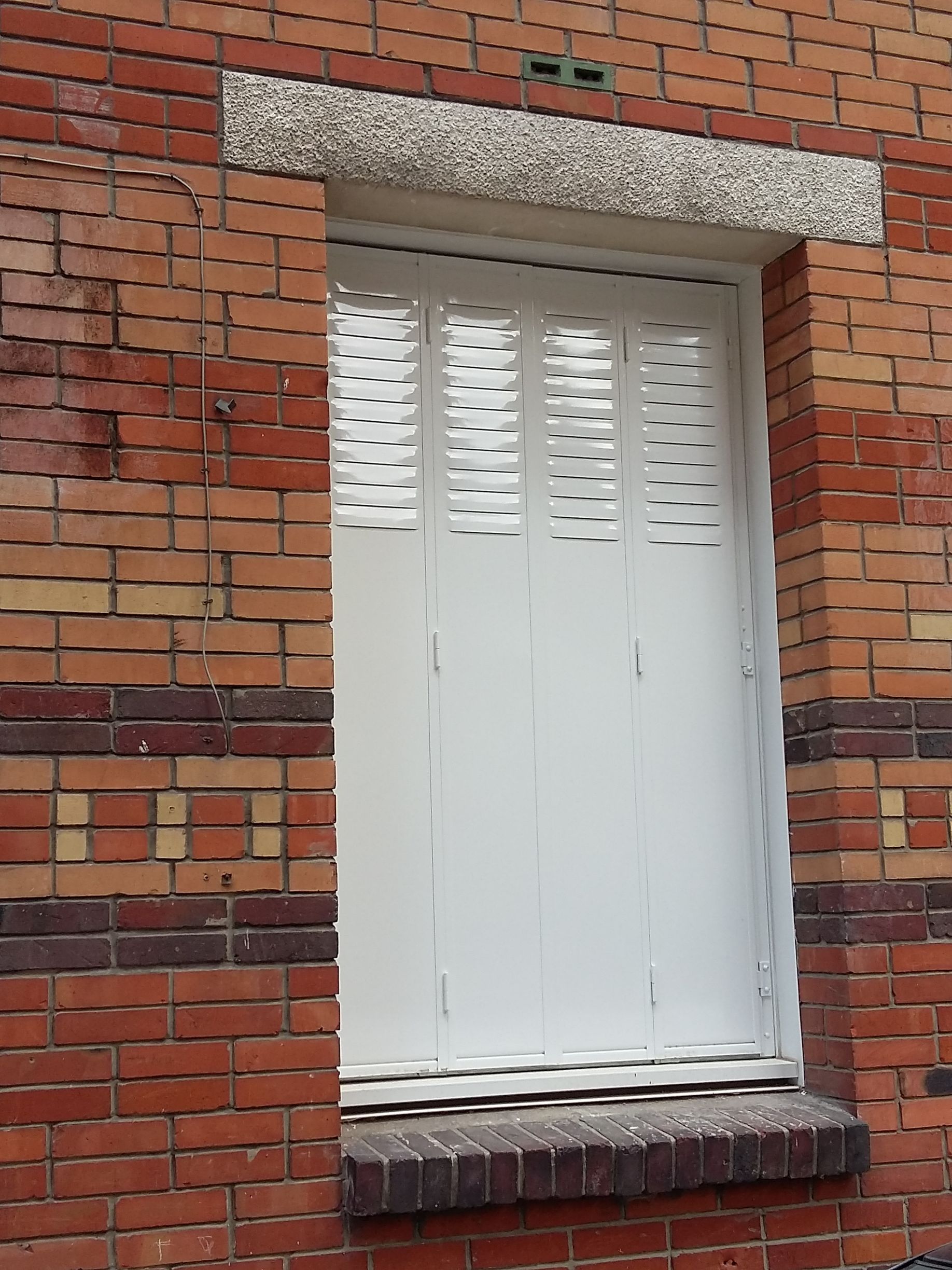 Volet blanc en accordéon et mur en briques.