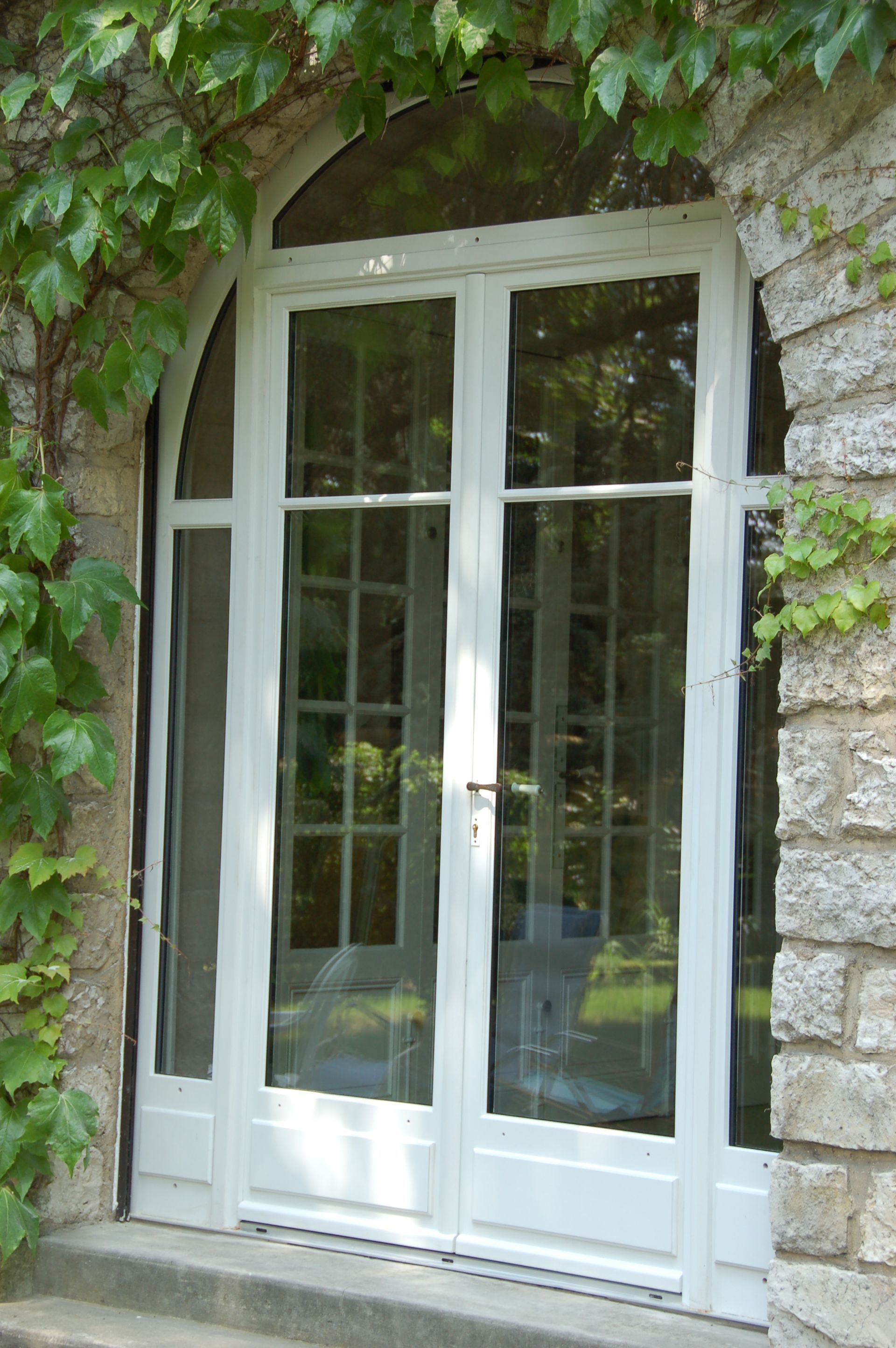Portes-fenêtres en verre à cadre blanc avec partie supérieure arquée et pierres grimpantes en lierre.