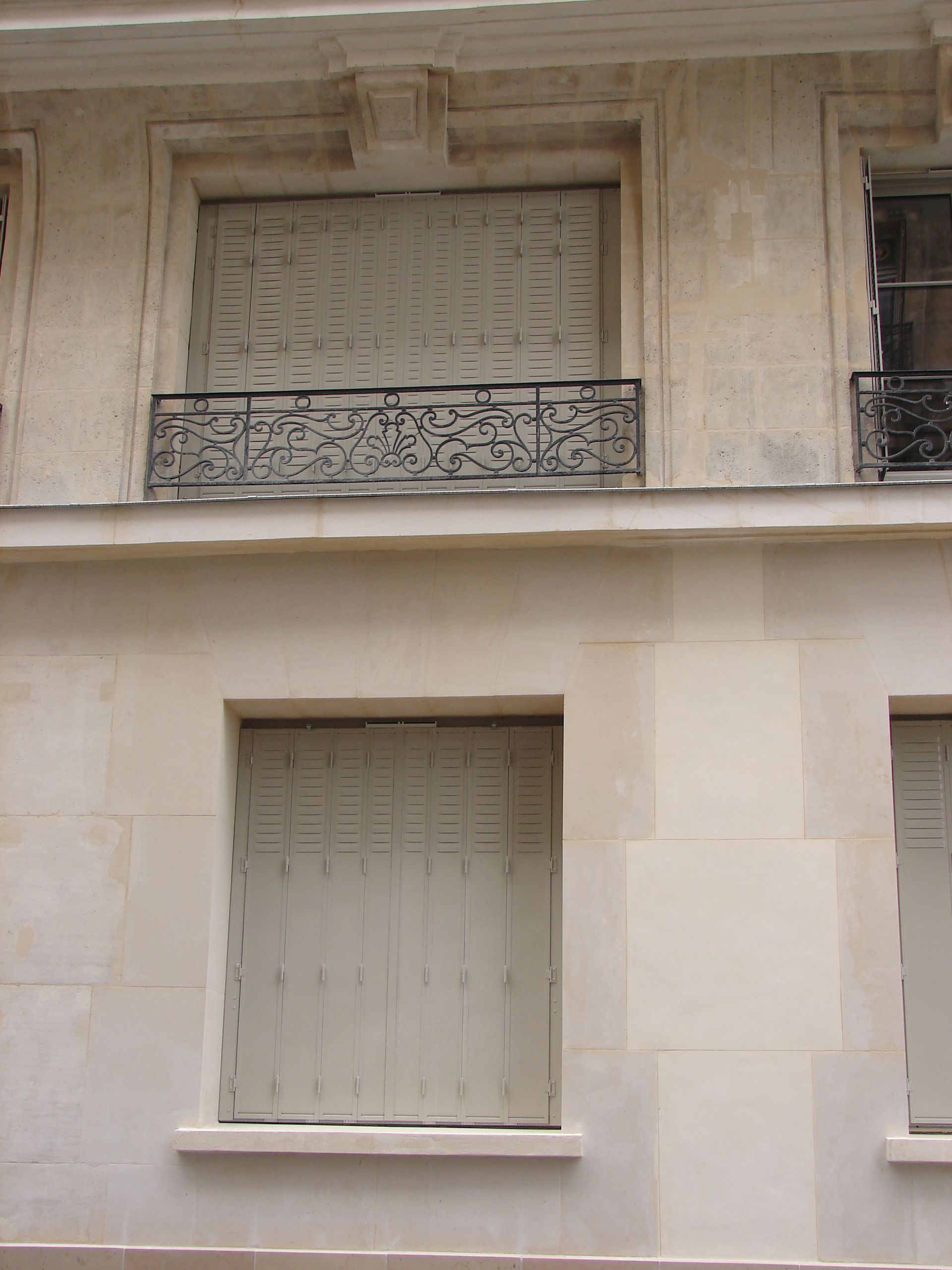Façade de bâtiment beige avec des fenêtres fermées et un balcon en fer forgé.