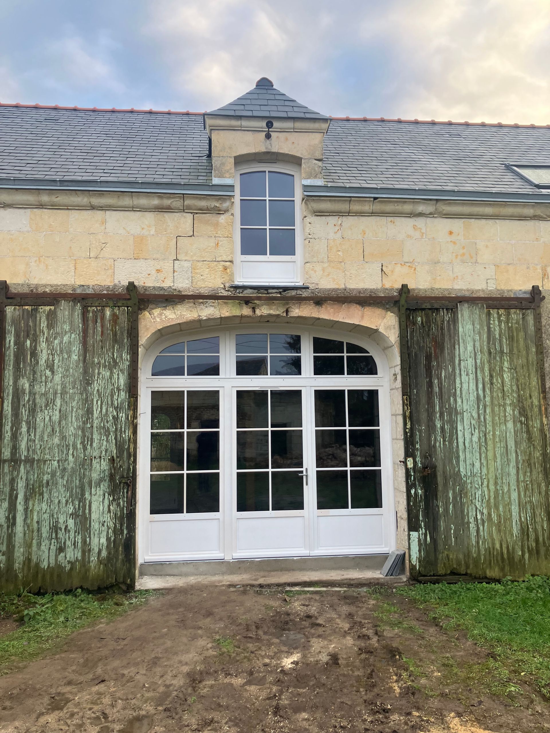 Bâtiment en pierre avec une grande porte blanche cintrée et une petite fenêtre supérieure.