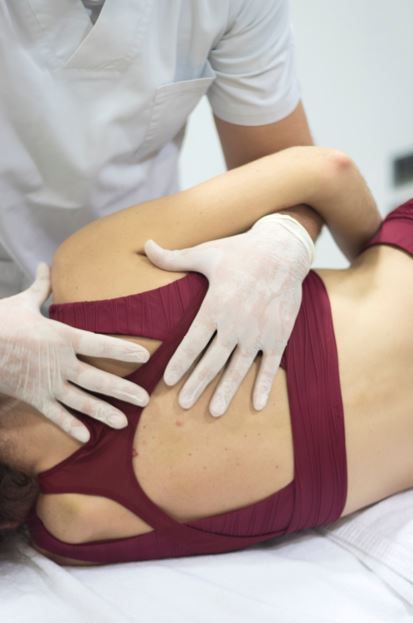 Una persona que recibe fisioterapia con las manos de un profesional de la salud en su espalda, usando cinta deportiva roja.