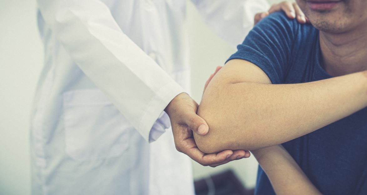 Médico examinando el codo de un paciente; tonos de piel claros, entorno médico.