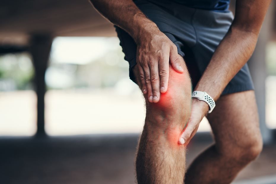Hombre agarrándose la rodilla, indicando dolor; resaltado rojo sobre la rodilla.