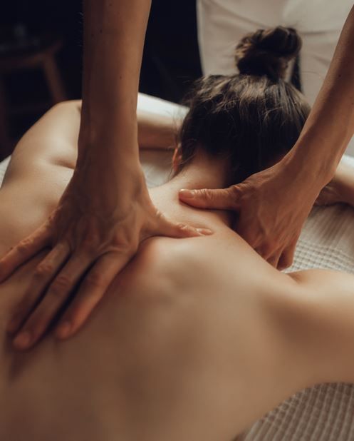 Manos masajeando la parte superior de la espalda y el cuello de una persona en una mesa de masajes.