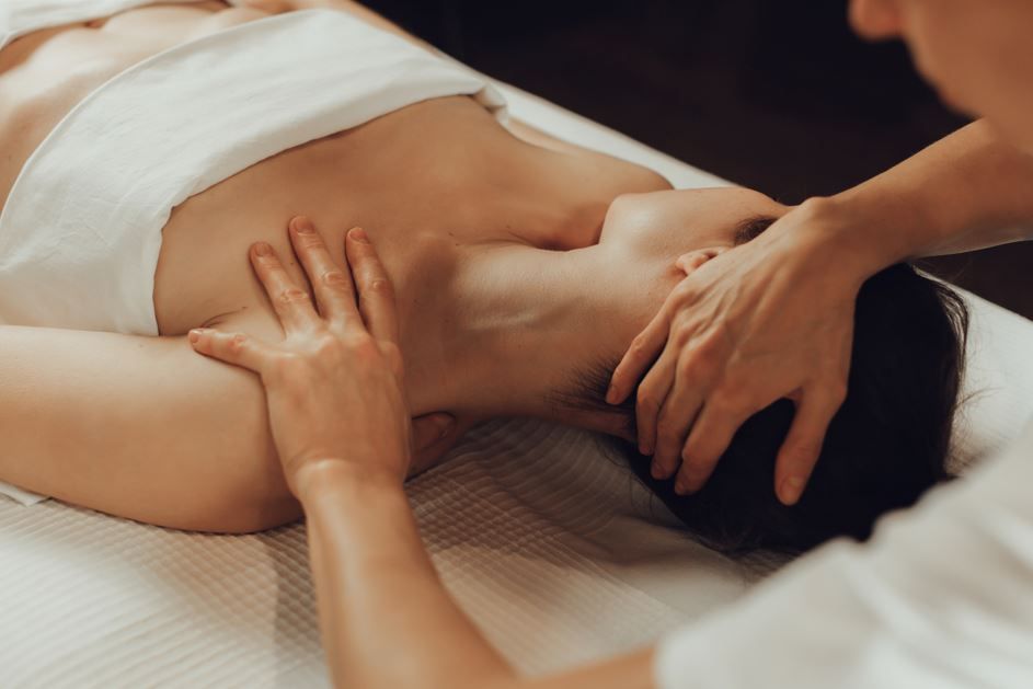 Persona recibiendo masaje de cuello y hombros, boca abajo en la camilla. Manos de la masajista trabajando.