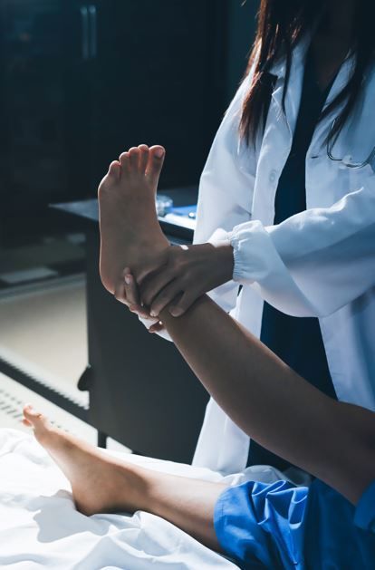 Un médico con bata blanca examina la pierna de un paciente, estirándola hacia arriba.