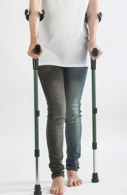 Persona que usa muletas, de pie en el interior, vestida con camisa blanca y jeans, descalza.